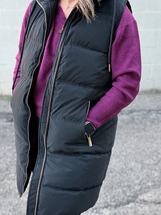 Person wearing a black puffer vest over a purple sweater with a blurred background